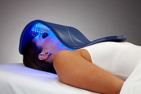 Woman lying down receiving Celluma LED light therapy treatment for acne on face and neck, using blue light technology