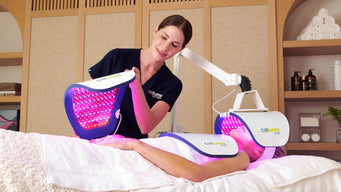 Esthetician placing a panel onto a clients hands while they lie on a massage table with additional panels over their neck/chest and face from the Celluma ELITE device.