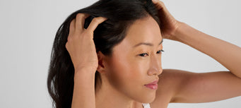Woman examining her hair, illustrating stress-related hair thinning and hair growth concerns discussed in red light therapy research