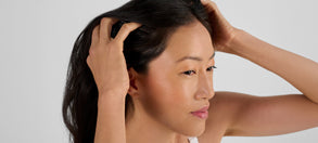 Woman examining her hair, illustrating stress-related hair thinning and hair growth concerns discussed in red light therapy research