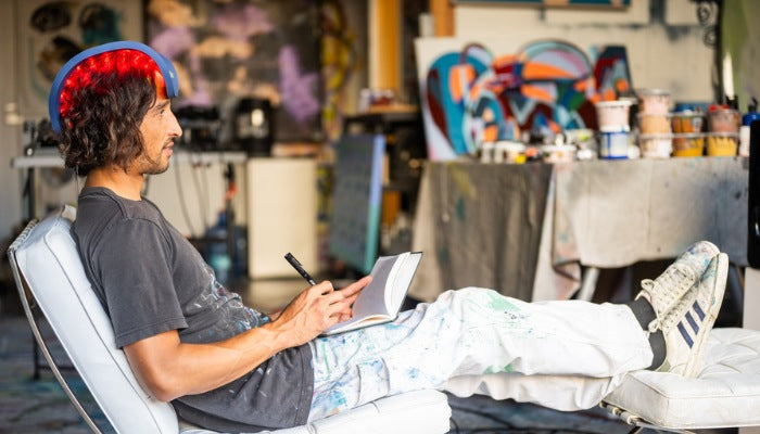 Young man reclining on a chair, drawing in a sketchbook with the Celluma panel on his head.