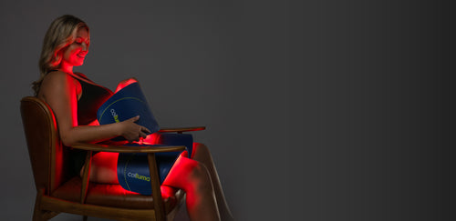 Woman sitting in chair receiving a LED red light therapy body contouring treatment on her thighs and abdomen using a Celluma CONTOUR PLUS multi-panel LED device.