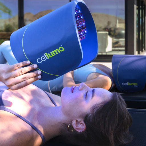 Young woman laying on a massage table about to lower a Celluma PRO LED red light therapy device onto her face for a skin treatment