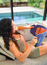 Woman sitting on couch with a Celluma  CONTOUR red light therapy LED device designed for body contouring. Red and near infrared light cast a warm glow on the body.