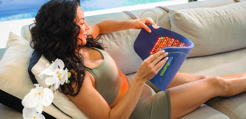 Woman sitting on couch with a Celluma  CONTOUR red light therapy LED device designed for body contouring. Red and near infrared light cast a warm glow on the body.
