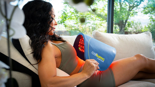 Woman on a couch shaping a Celluma LED light therapy device on her abdomen for a body contouring treatment