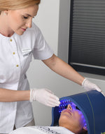 Aesthetician using a Celluma light therapy device on a client's face during a skincare treatment.