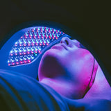 Woman lying under a Celluma LED device receiving a facial treatment with a combination of blue, red, and near infrared light therapy.